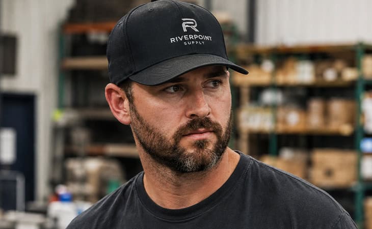 Employee wearing a black branded embroidered baseball cap in a warehouse workspace