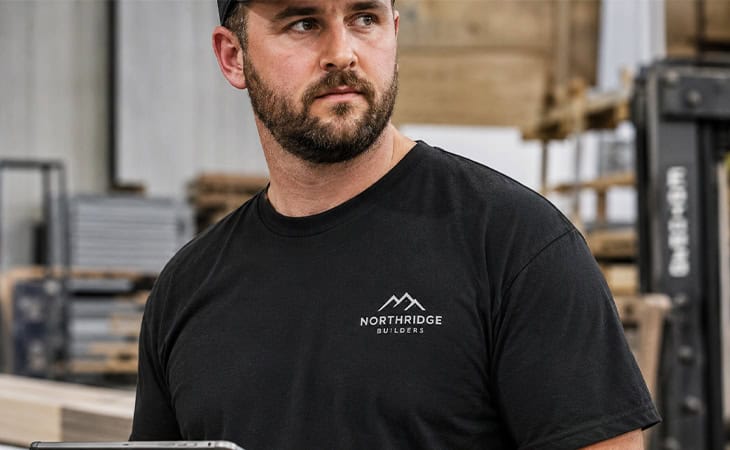 Workshop foreman reviewing custom branded T-shirt samples on a tablet in a professional apparel production workspace